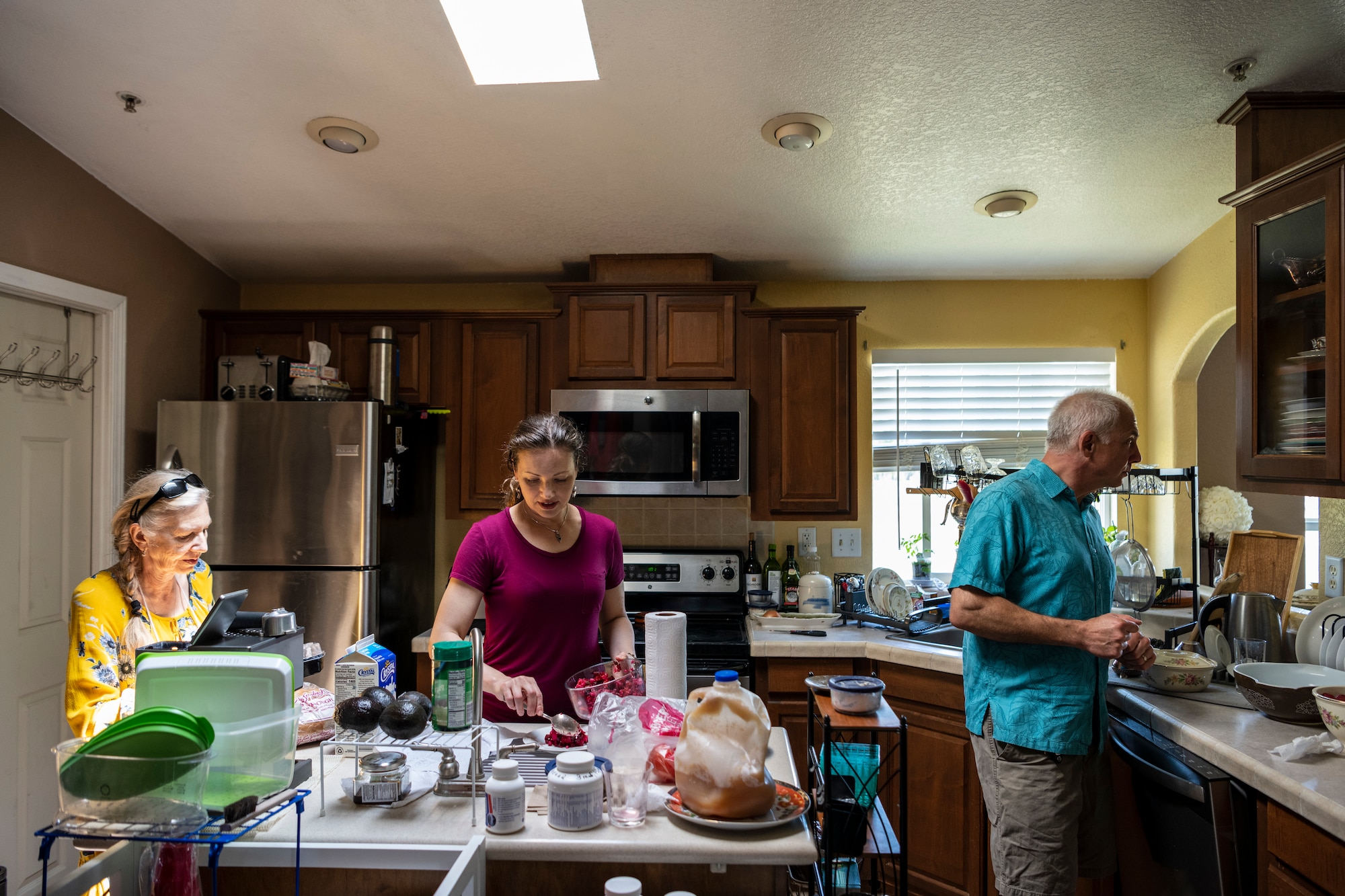 Two women and a man stand in a kitchen.