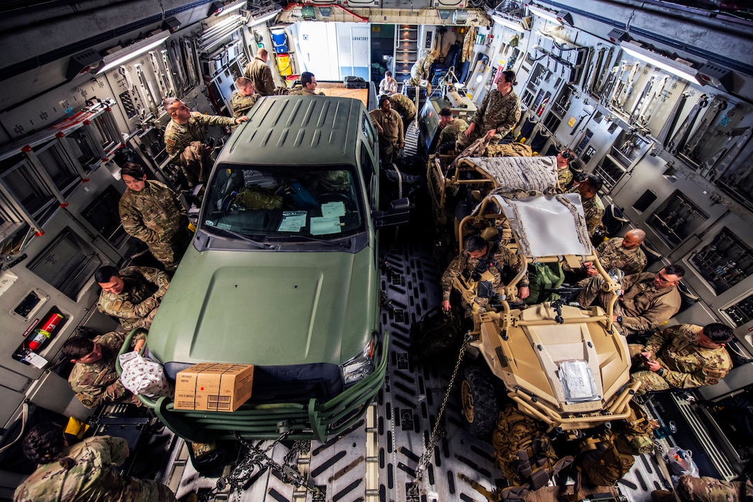 A group of service members and two military vehicles are in the cargo hold of an aircraft.