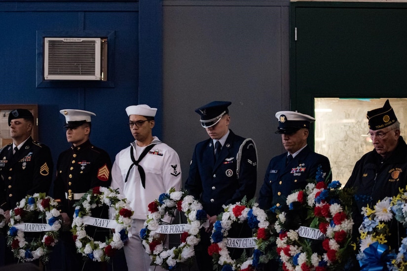 Six service members stand behind a line of wreaths