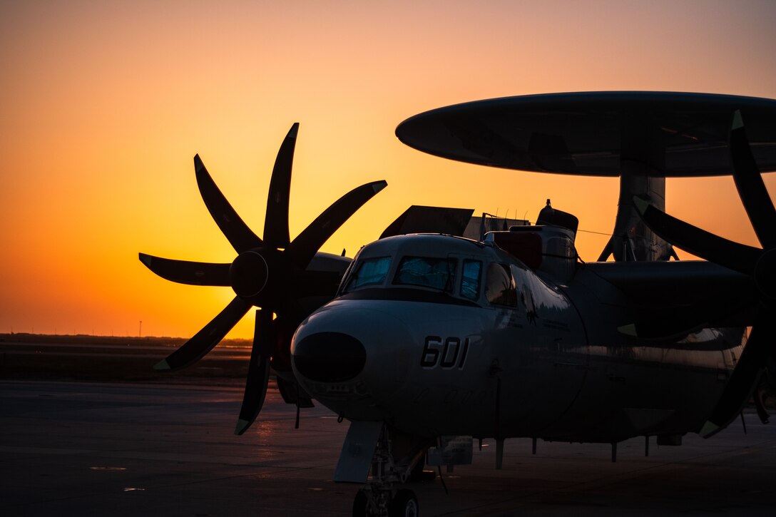 A Navy aircraft sits on tarmac during a sunset.