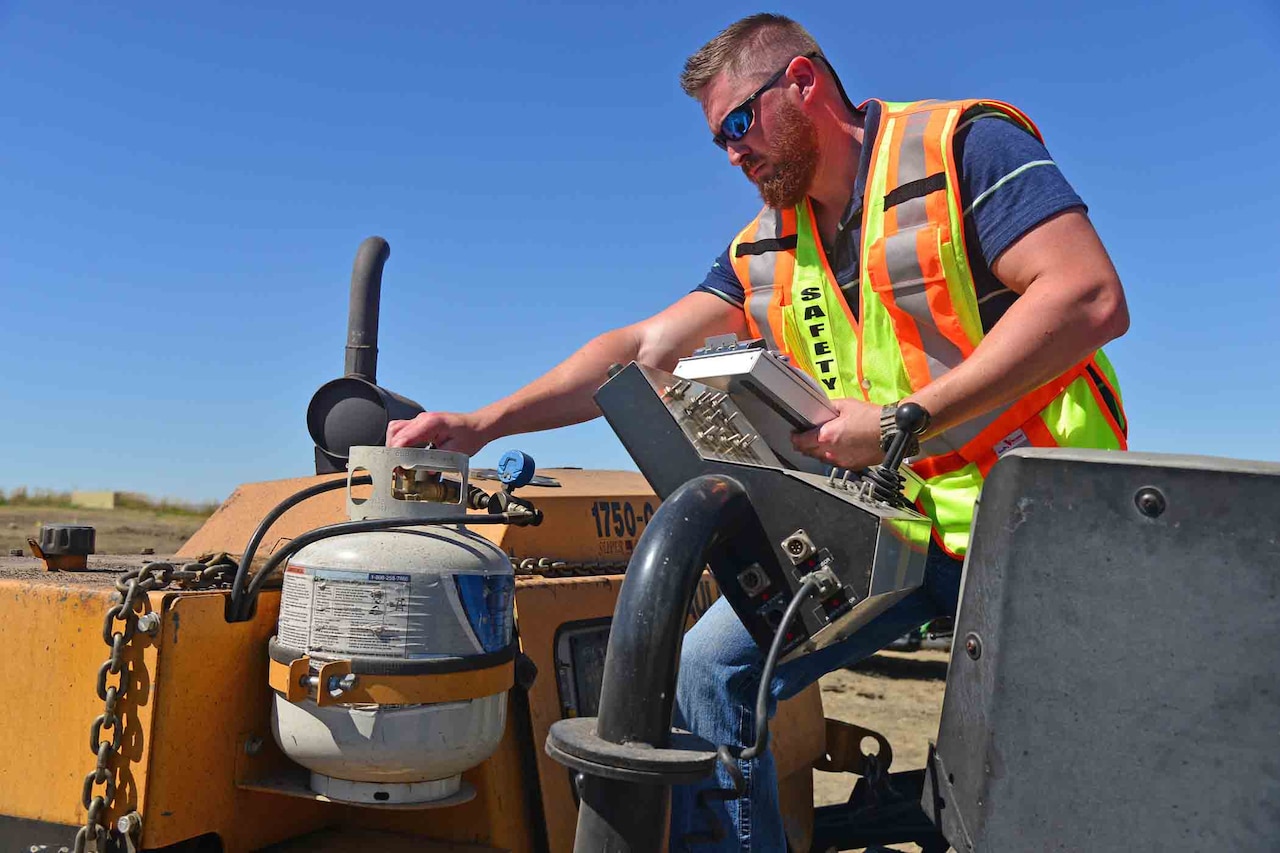 A man wearing an orange construction vest twists a valve on a pressurized tank.