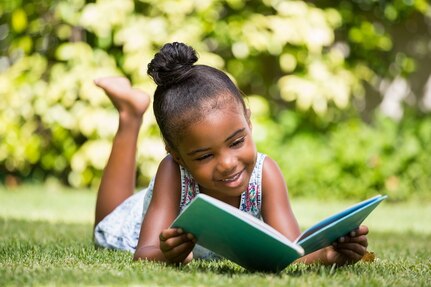 Young girl reading a book outdoors.
