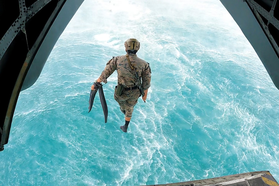 A Marine jumps from an aircraft toward a body of water.
