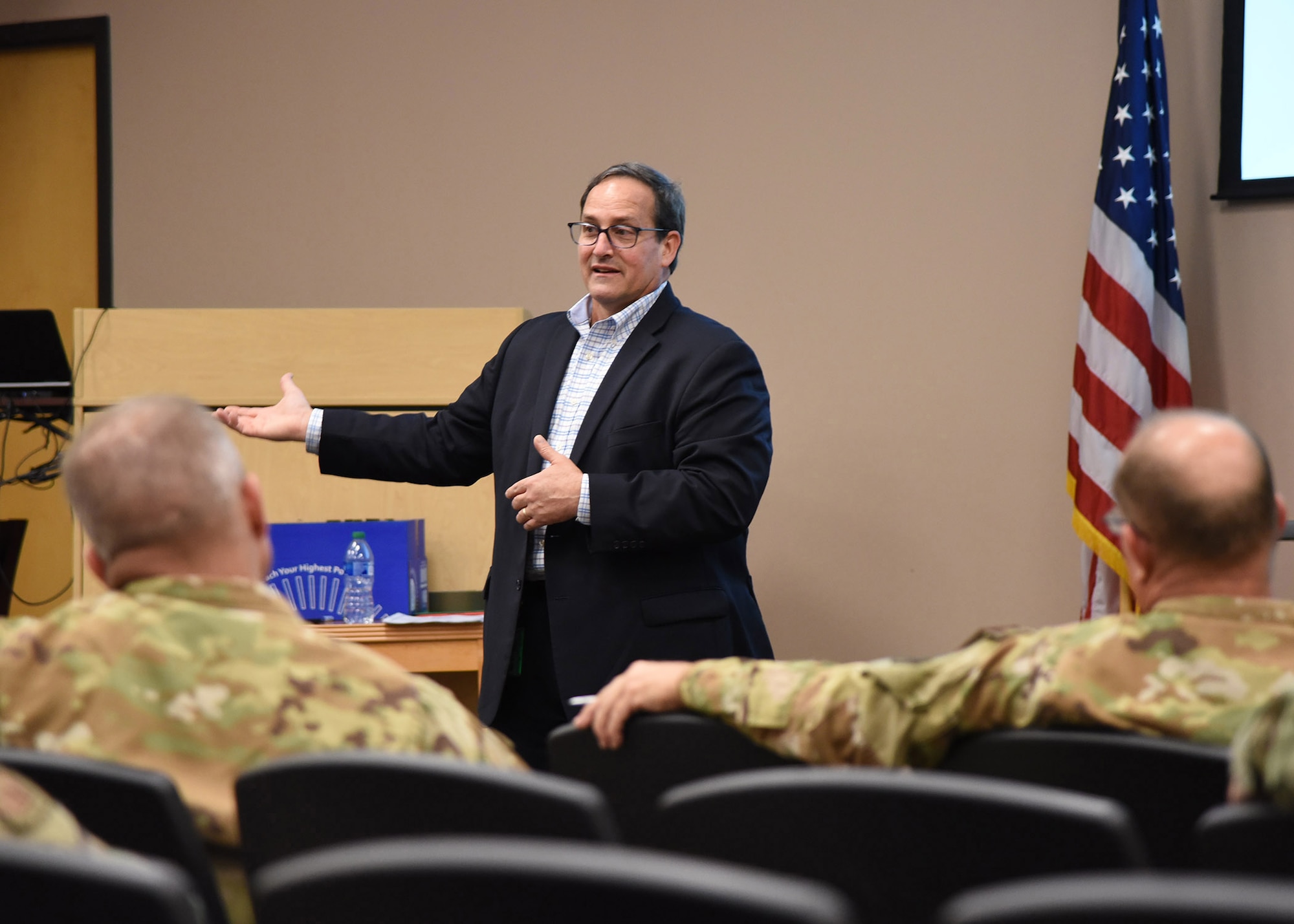 A man in gestures while speaking to a room full of Airmen