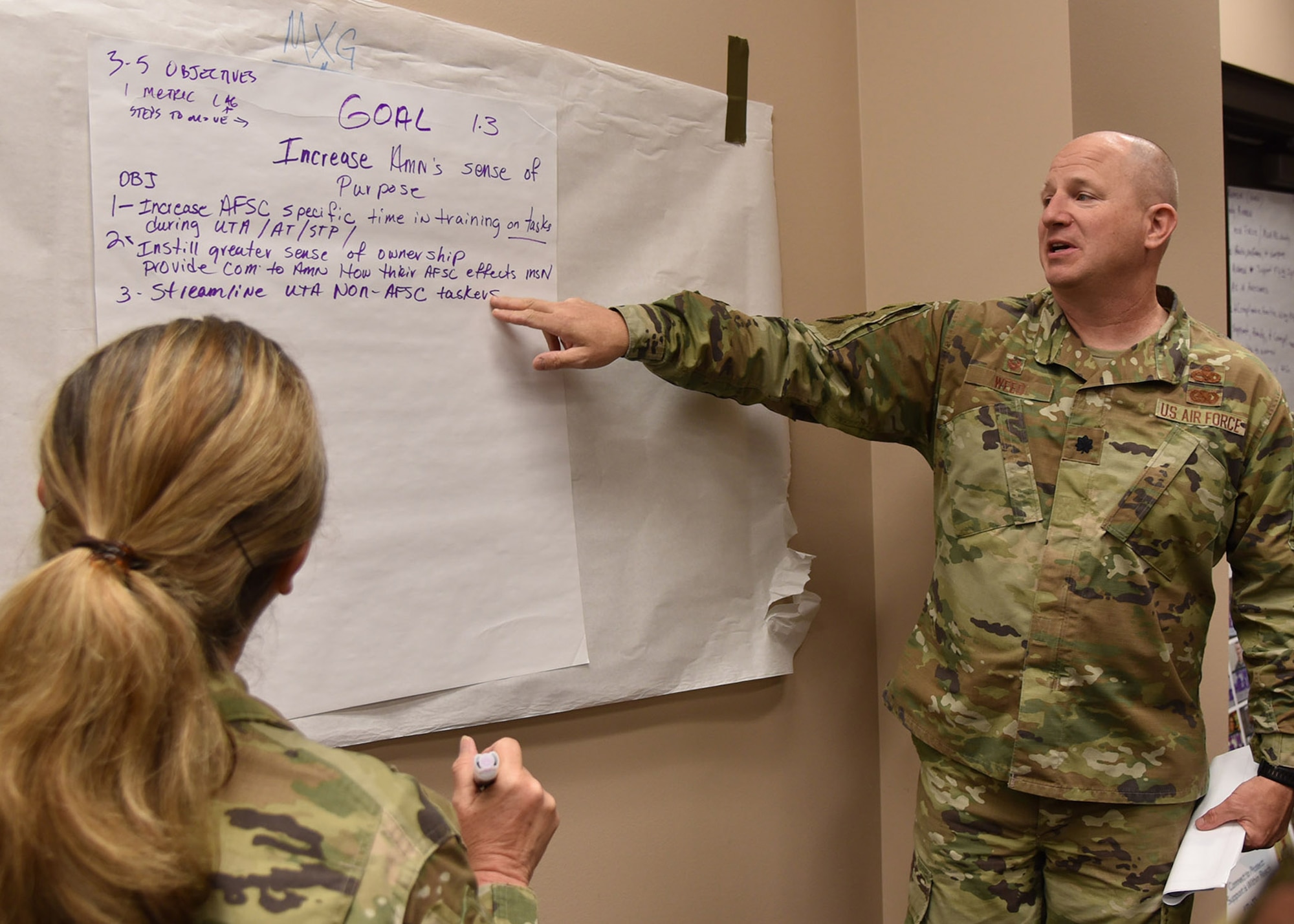 Lt. Col. Weed points to a paper on the wall as SMSgt Trippe looks on from the foreground