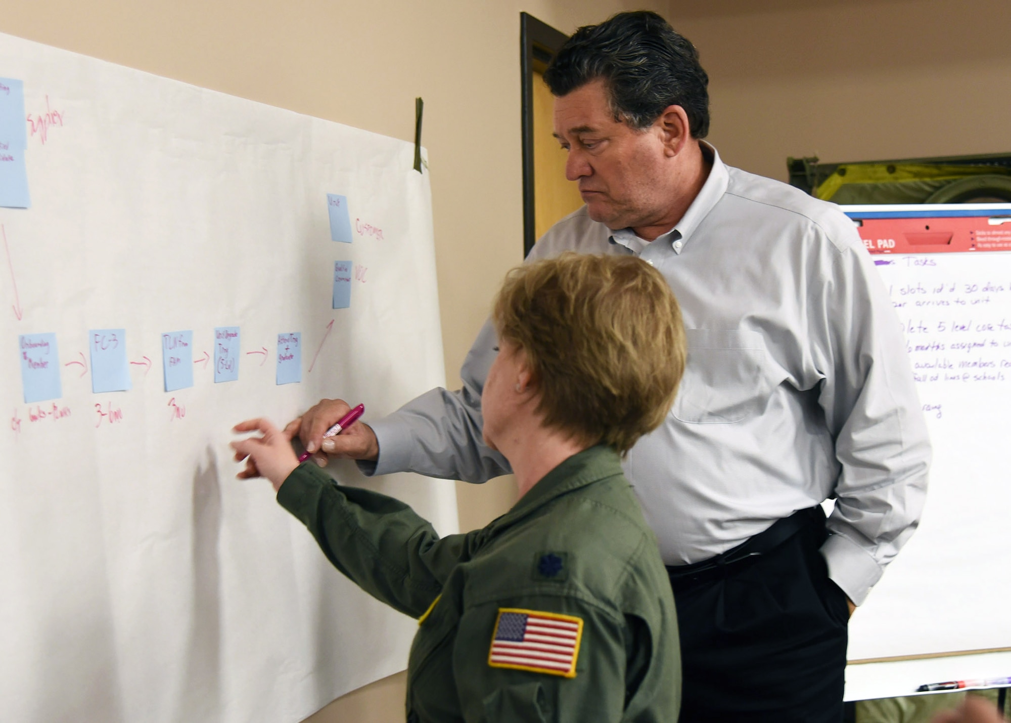 A man and Airman write on a large sheet of paper on the wall