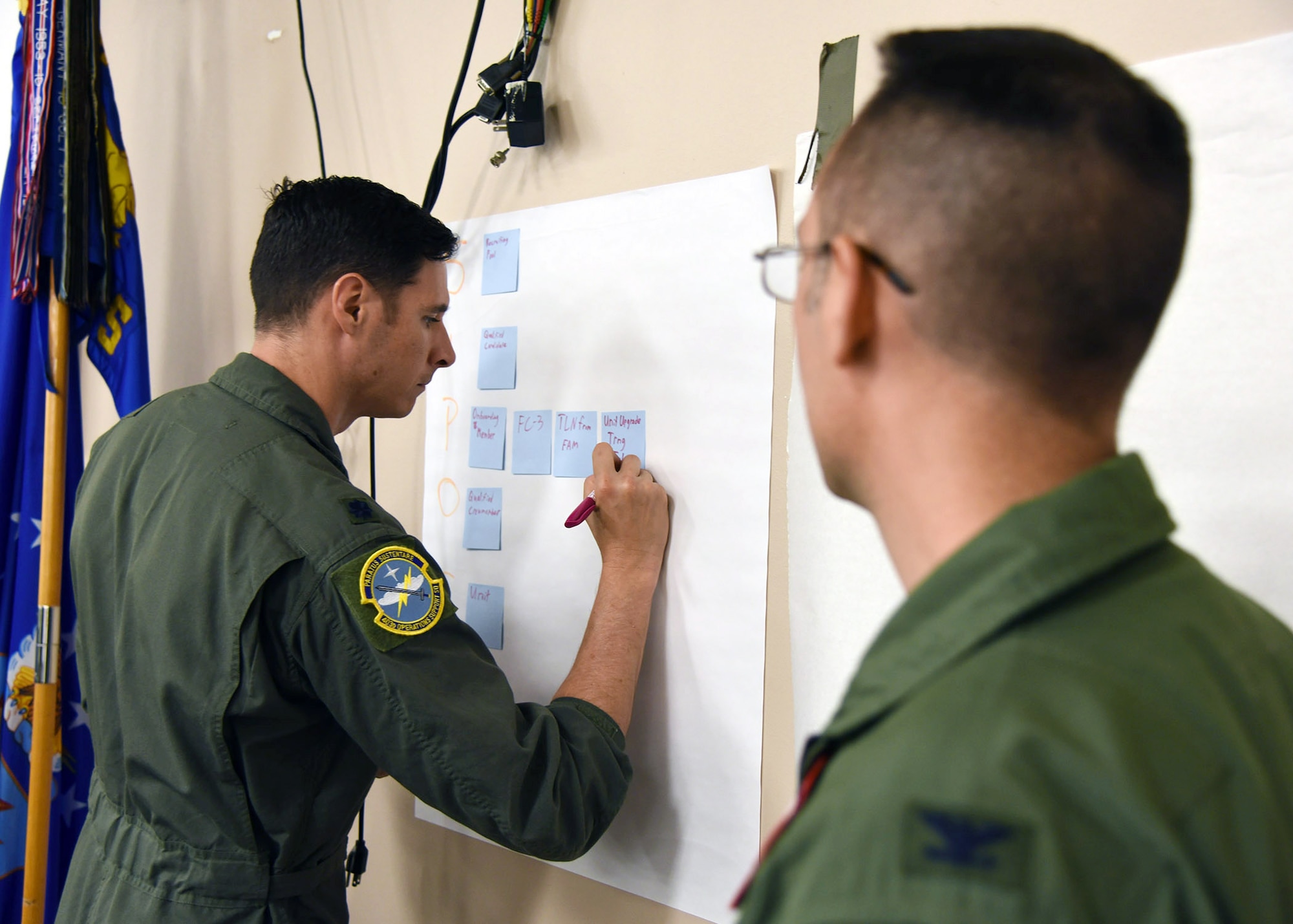 Lt. Col. Gentile adds notes to a paper on the wall while Col. Campanile looks on