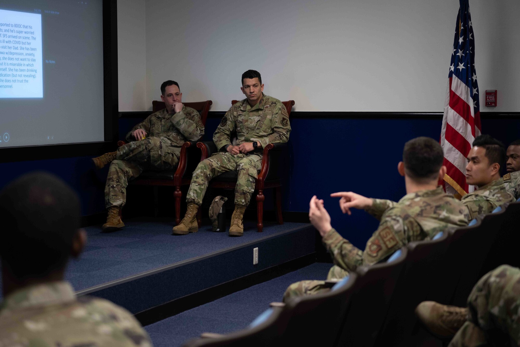 Two military members sit as another explains to a room an experience.