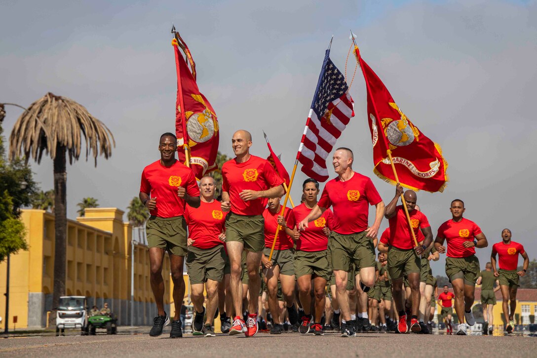 A group of Marines run together, some carry flags.