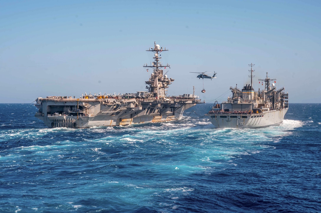 A helicopter flies between two ships at sea.