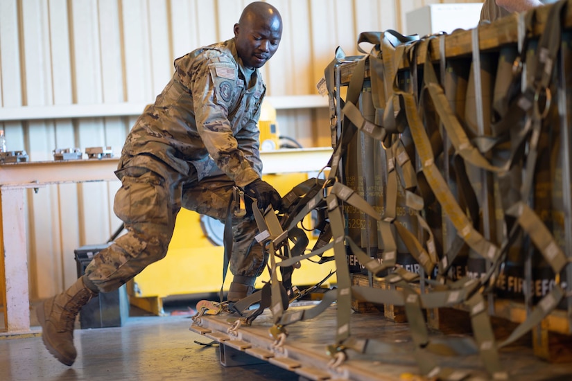An airman secures pallets with rope in a warehouse.