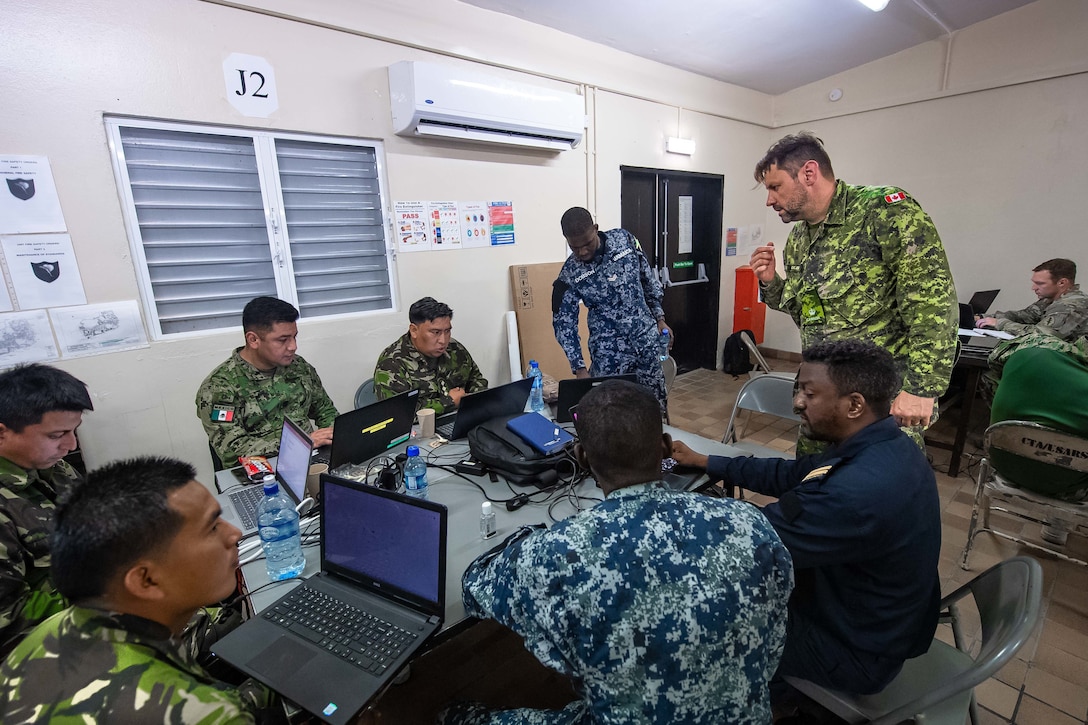 Military personnel speak to each other in front of a computer.