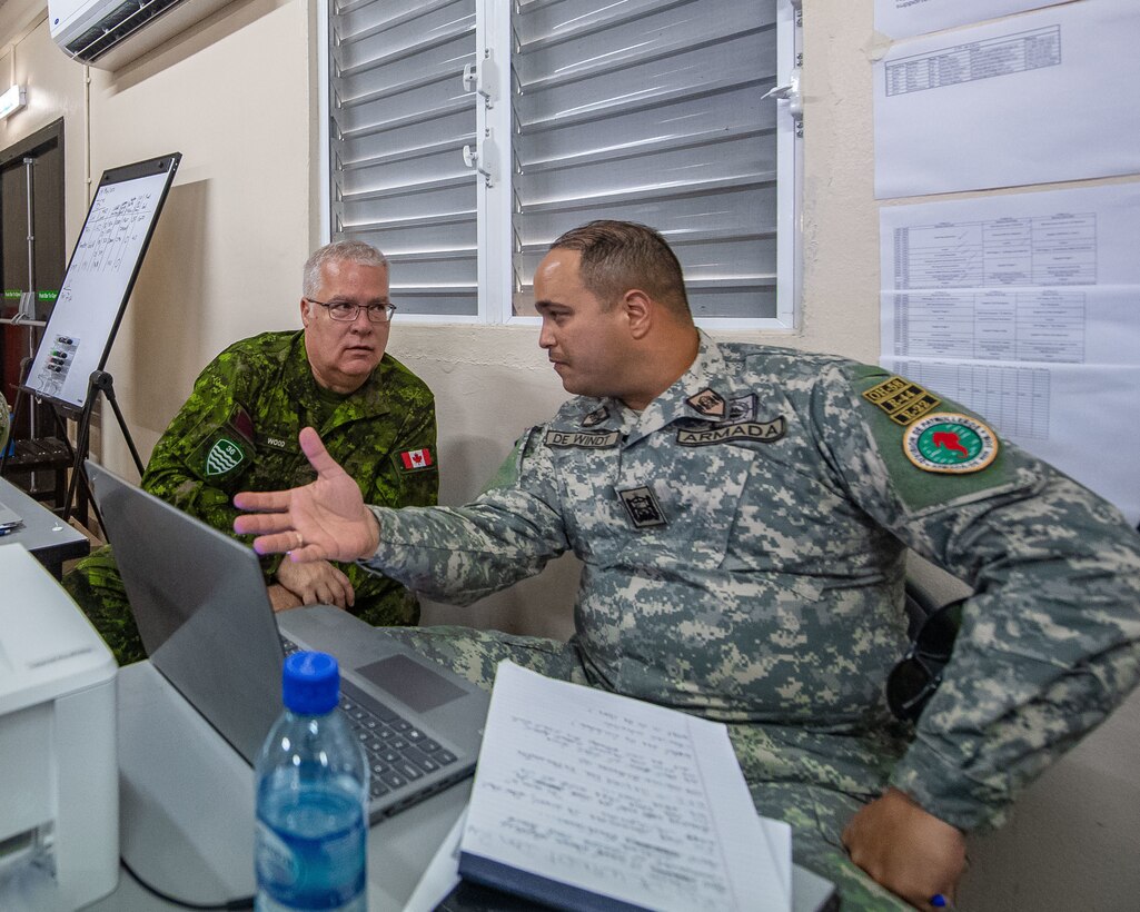 Military personnel speak to each other in front of a computer.