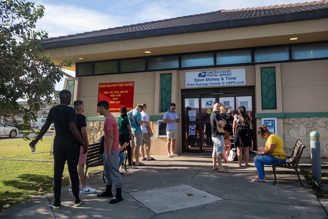 Several people stand in line outside a U.S. post office.