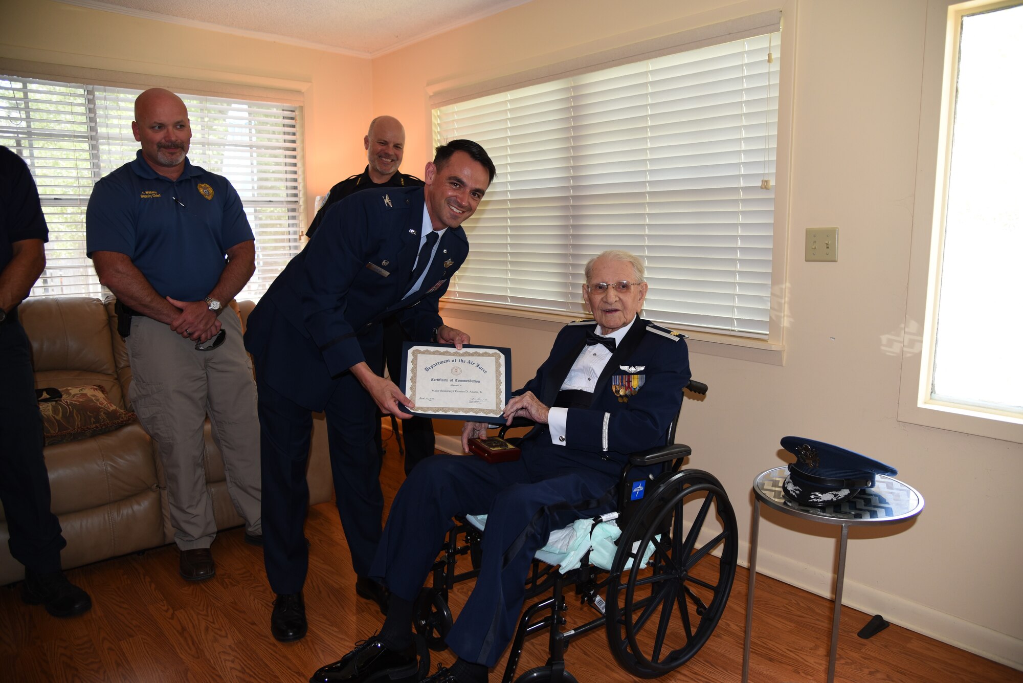 Col. Rubio bends down to present a certificate to Maj. Dewey, sitting. Onlookers are in the background