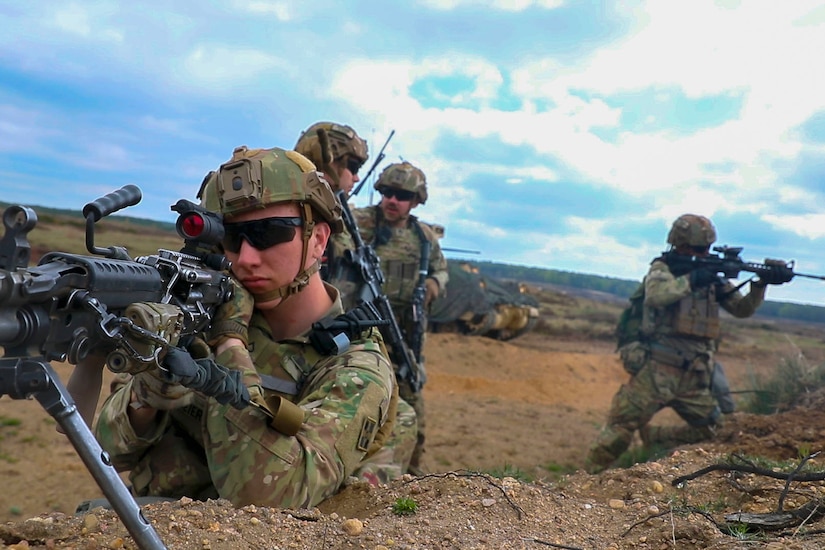 Two soldiers aim their guns while two other soldiers talk in the background.
