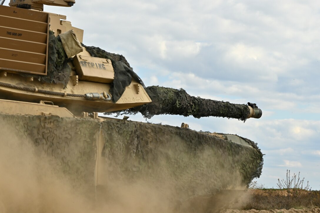 A tank covered with camouflage material moves out.