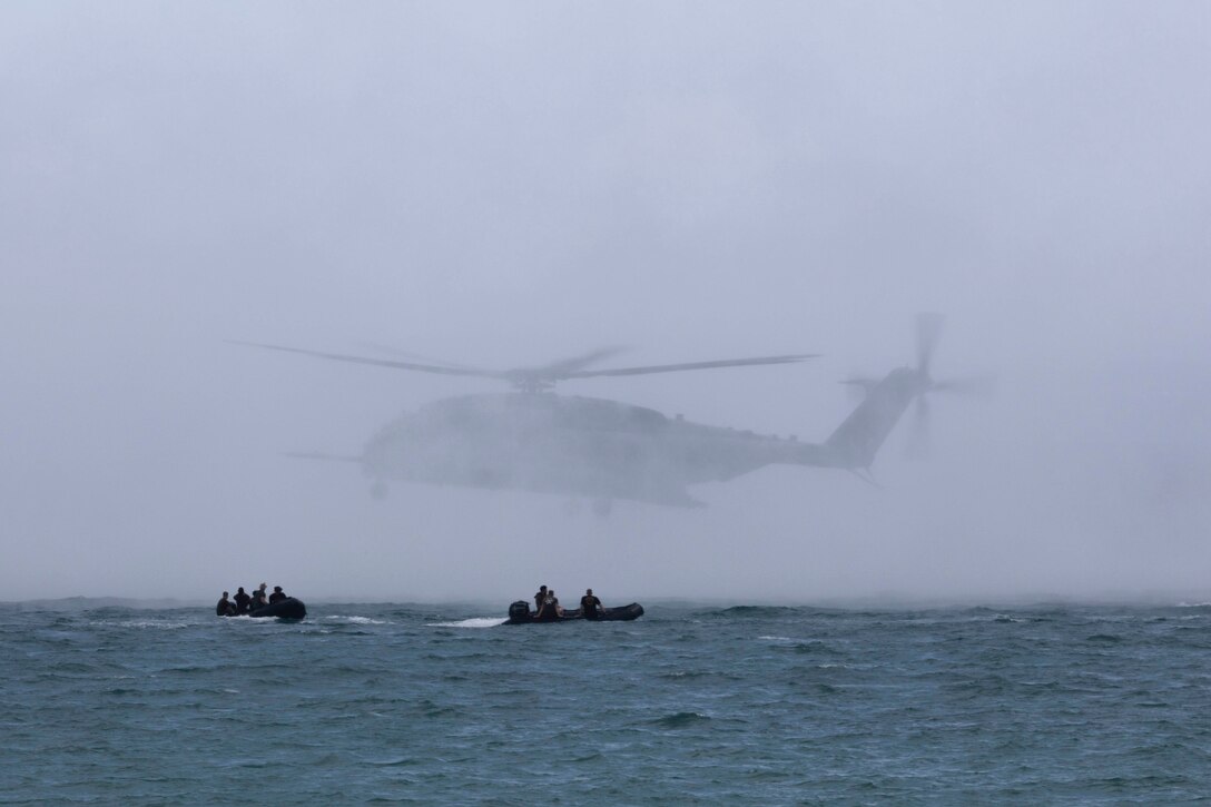 Marines travel waters in two small inflatable boats as a helicopter flies above.