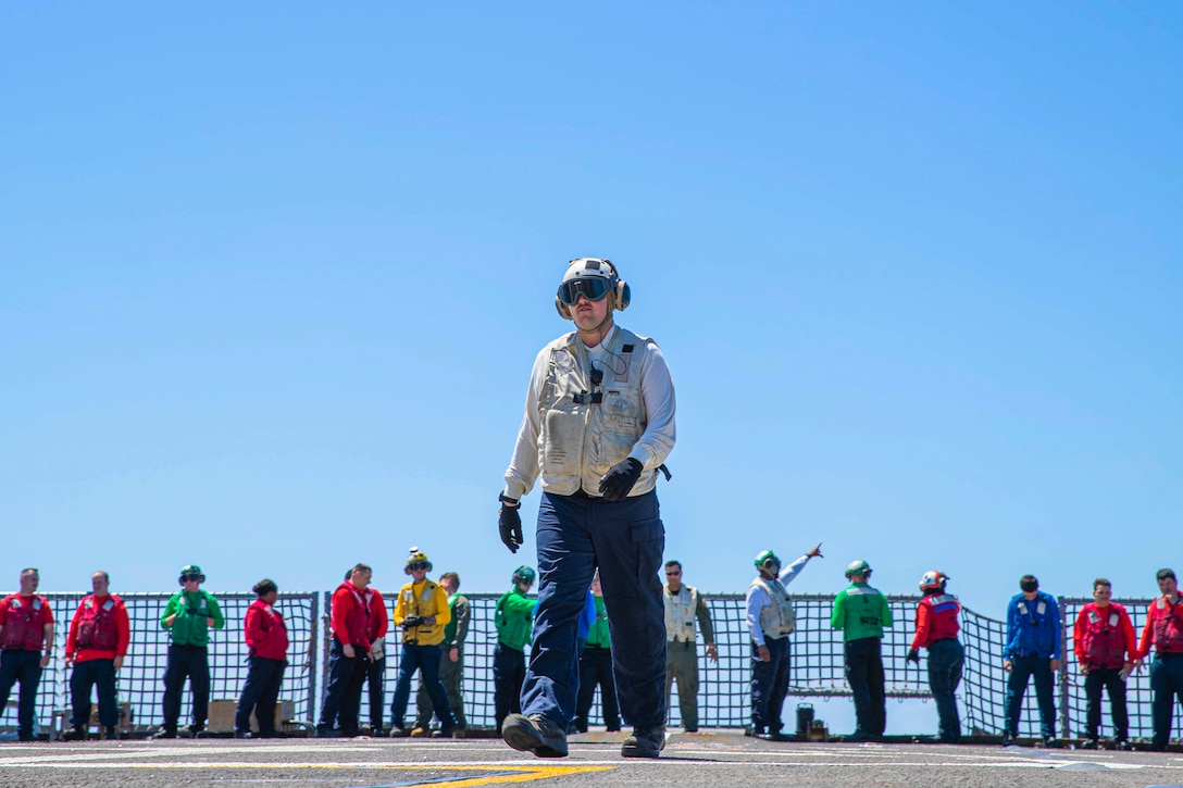 A sailor walks in front of a line of other sailors.