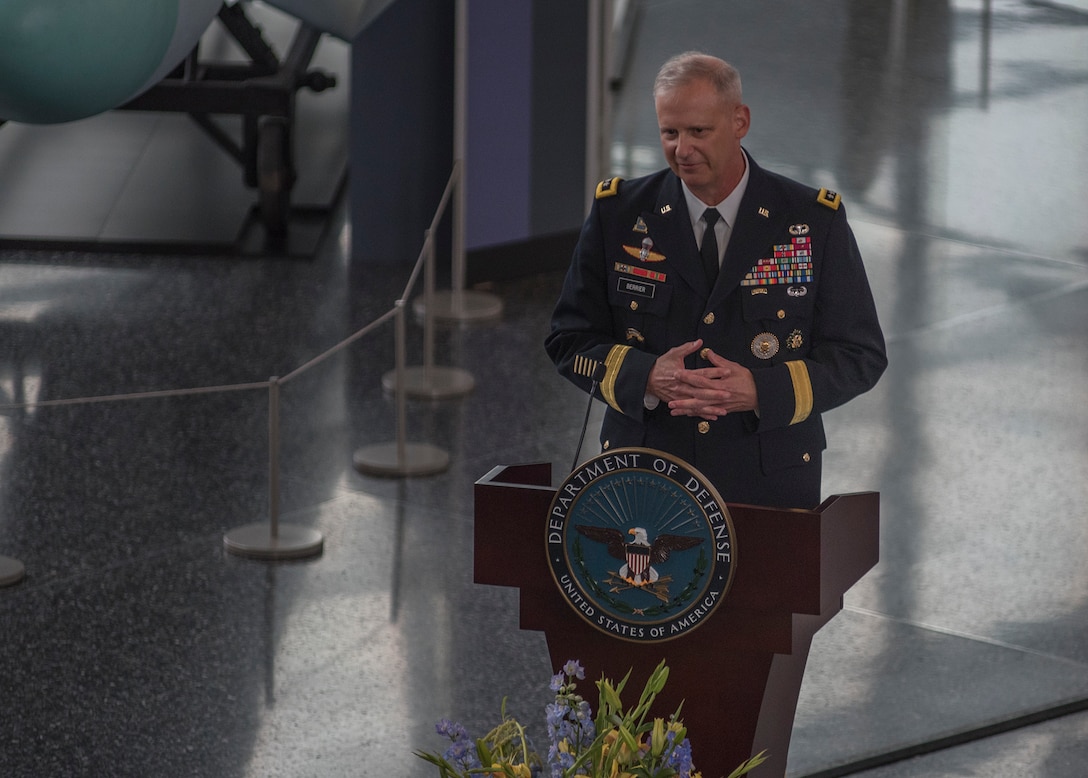 A man in a military uniform stands behind a lectern with a Defense Department logo.