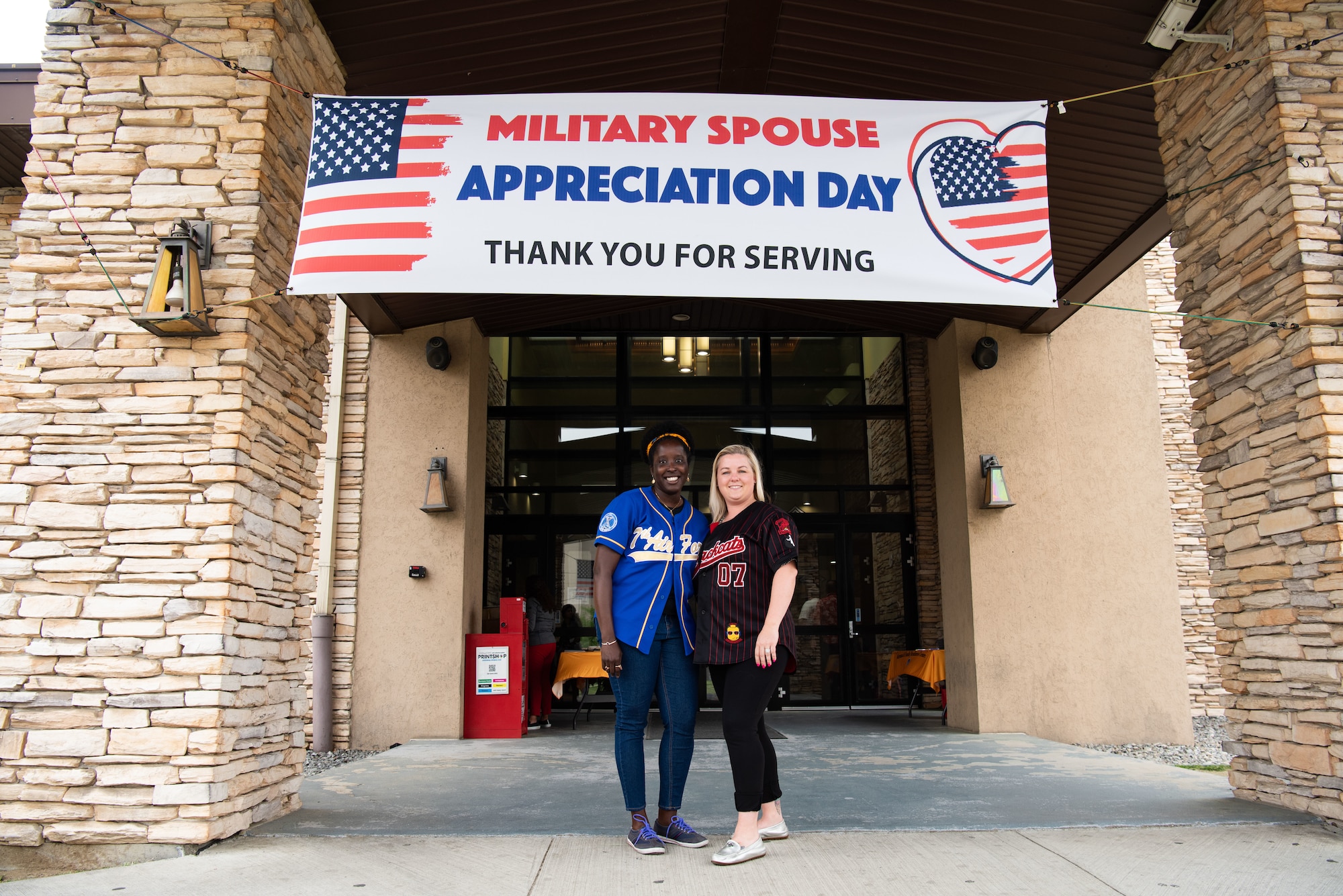 Two military spouses smile together underneath a military spouse appreciation day banner