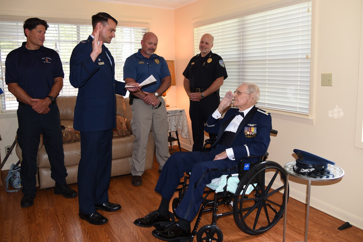 Col. Rubio, right hand raised, reads the oath of commission. Maj. Dewey, sitting, raises right hand. Three onlookers in the background