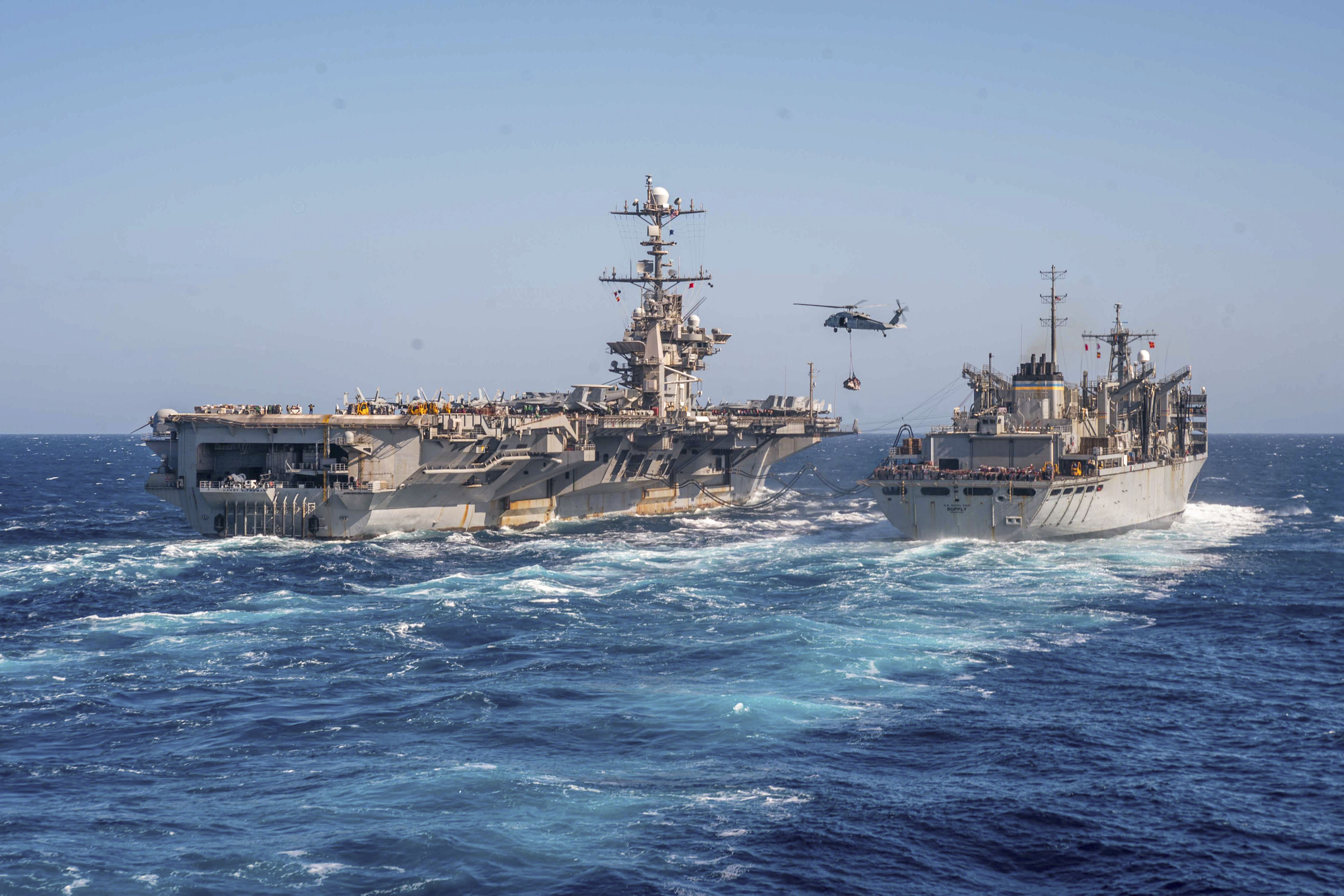 A helicopter flies between two ships at sea.