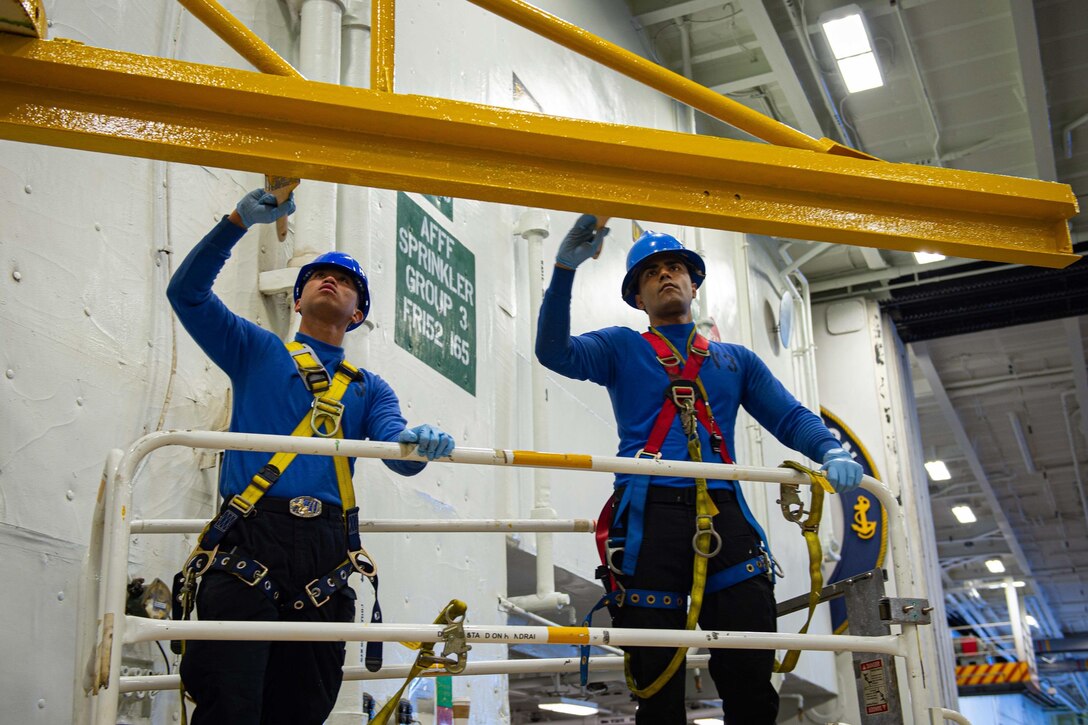 Two sailors paint a crane.