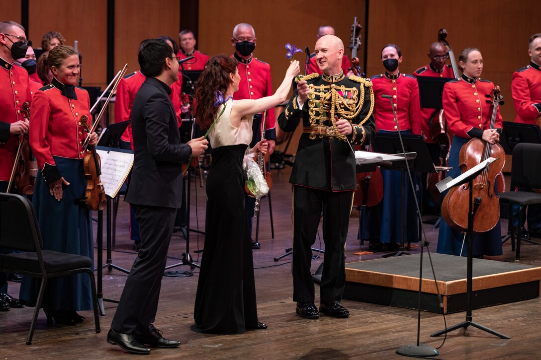 On May 8, 2022, guest soloist Mimi Stillman performed with the Marine Chamber Orchestra at the Rachel M. Schlesinger Concert Hall and Arts Center in Alexandria, Va. During the concert, she gave the world premiere of Concerto for Flute and Orchestra by composer Zhou Tian. As shown: Mimi Stillman offers Director Col. Jason K. Fettig an Iris after the world premiere of Zhou Tian's Concerto for Flute and Orchestra. The piece's opening movement was titled "Irises."