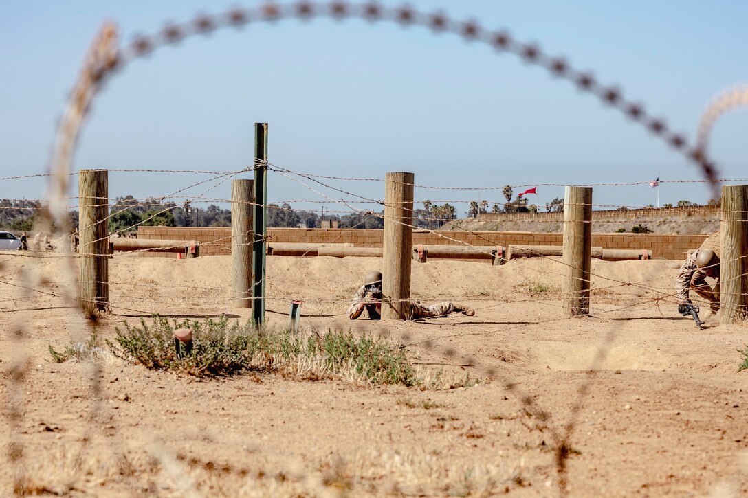 Marines with weapons train behind a barbed wire fence.