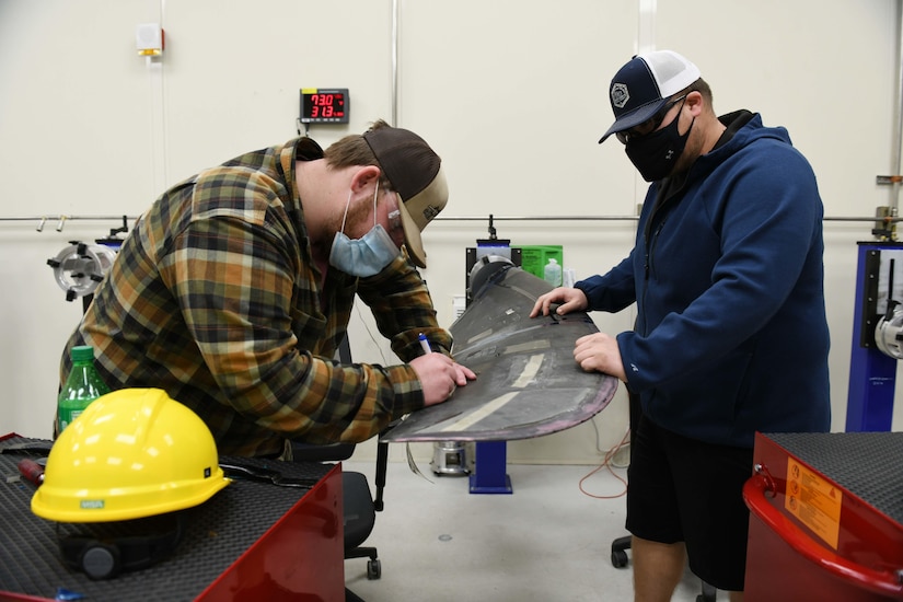 Two men manipulate a single propeller blade of an aircraft.