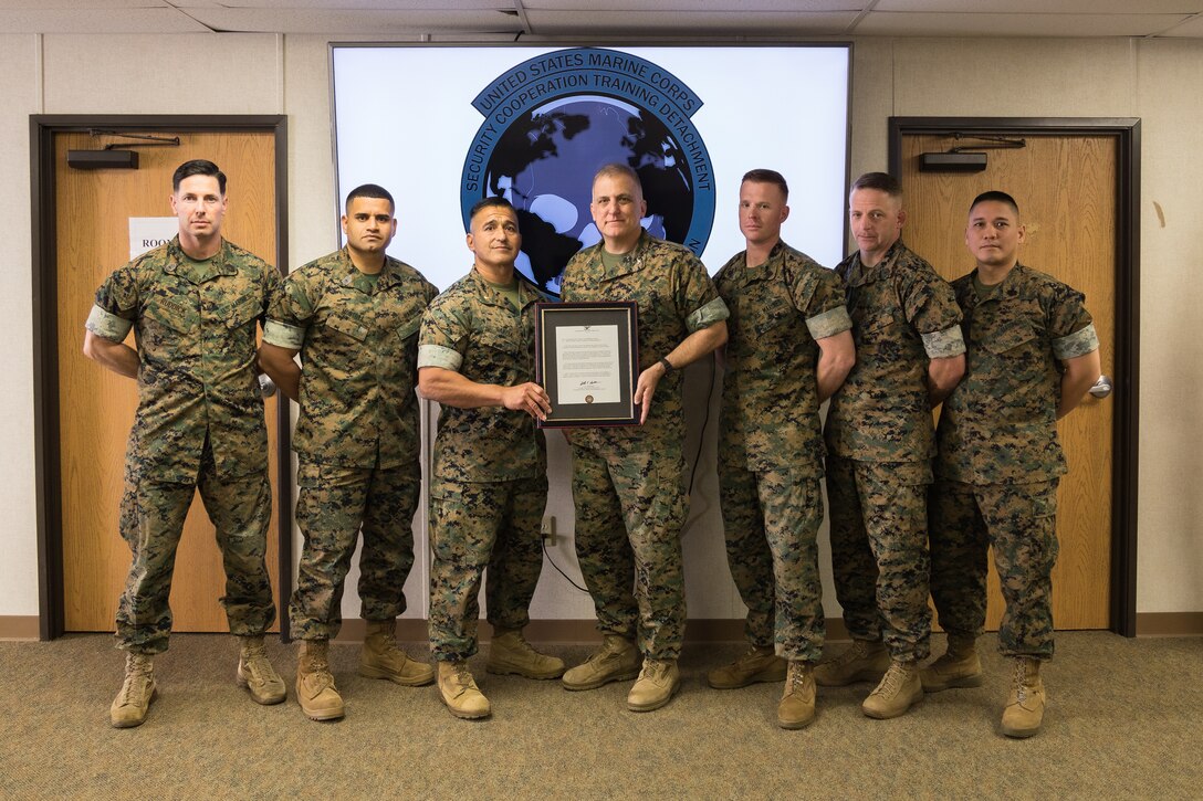 U.S. Marine Corps Col. Seth E. Anderson, the commanding officer of the Marine Corps Intelligence Schools, Training Command, center right, and Maj. Vic Garcia, officer-in-charge of Marine Corps Security Cooperation Training Detachment (MCSCTD), center left, gather with the MCSCTD staff at Joint Expeditionary Base Little Creek-Fort Story, Virginia, May 9, 2022. The ceremony formally activated MCSCTD following the deactivation of Marine Corps Security Cooperation Group on September 2, 2021. MCSCTD was established as part of the Force Design 2030 initiative to streamline the Marine Advisor Course and create an efficient pipeline for advisors trained to incorporate security cooperation into interoperability planning between the U.S. Marine Corps and its strategic partners. (U.S. Marine Corps photo by Casey Price)
