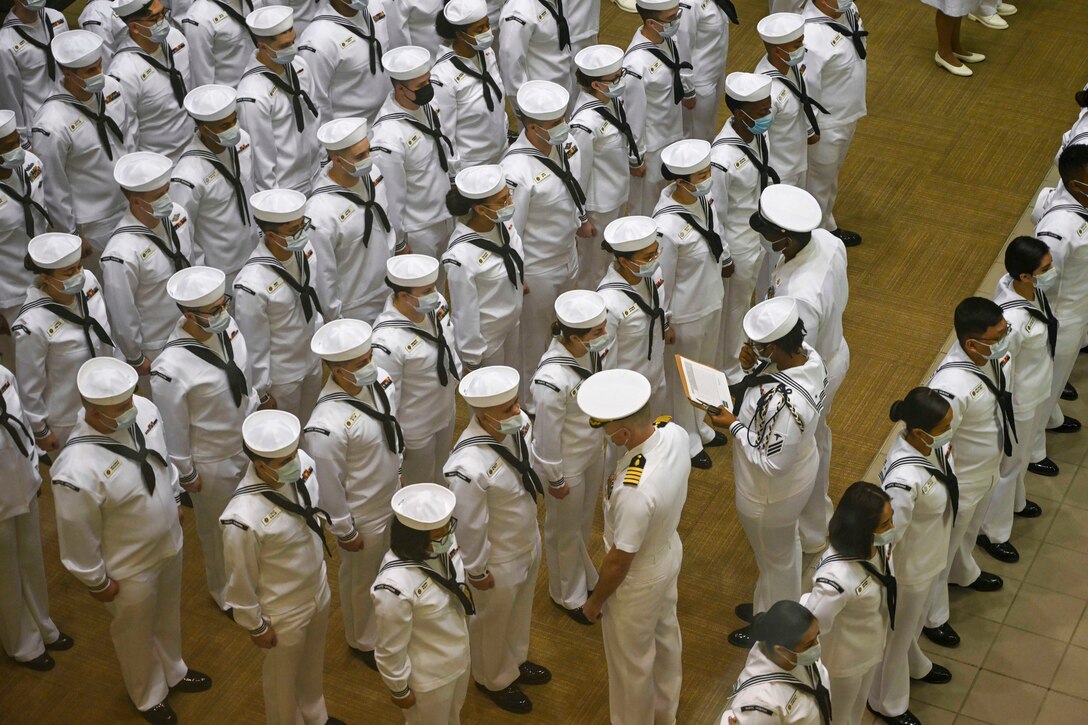 A large group of sailors wearing white uniforms get inspected.