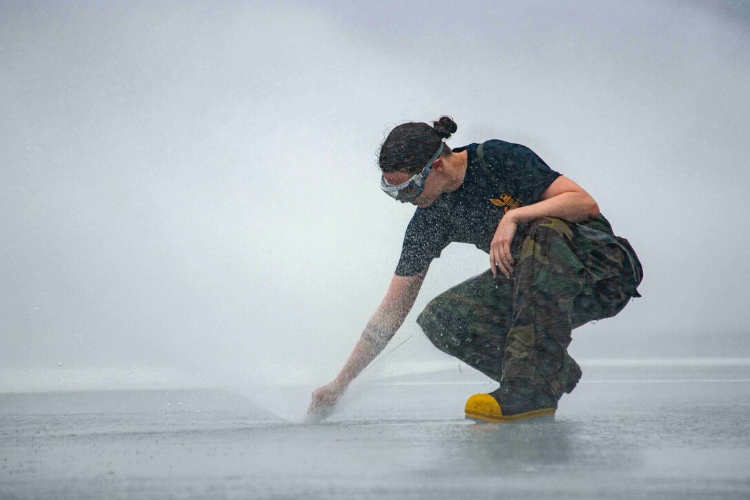 A sailor inspects a sprinkler as it sprays water.