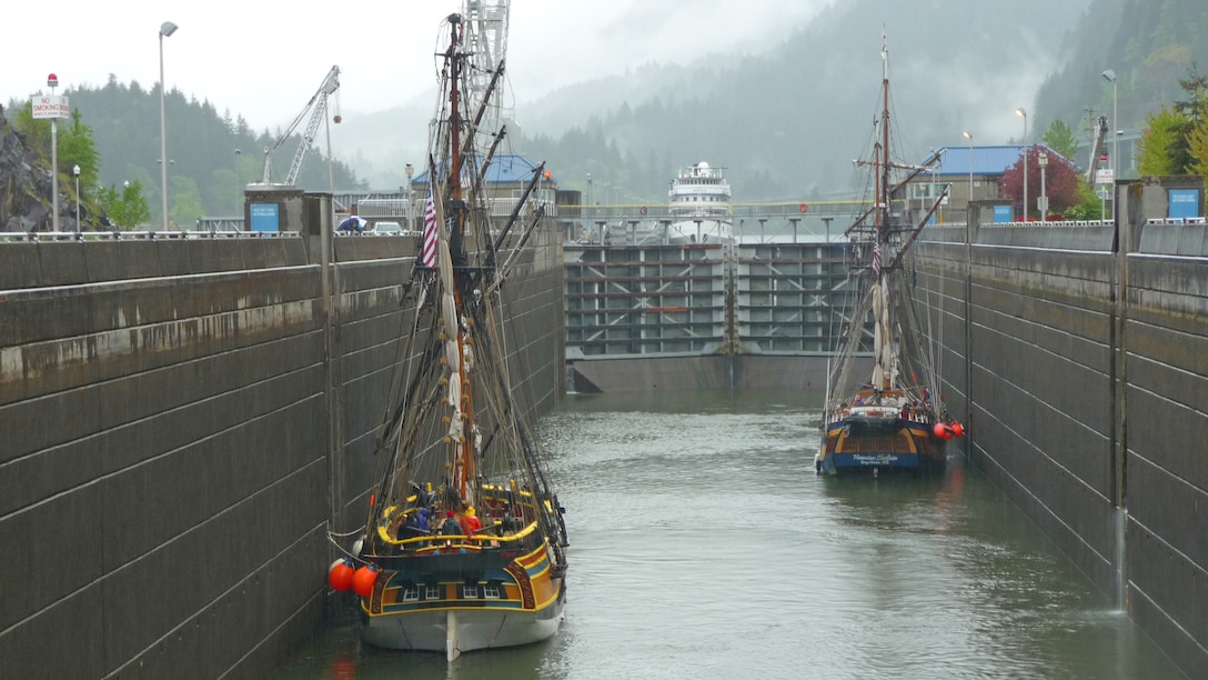 Two pirate ships sit in a massive concrete basin as the basin fills up with water. It is a bleak and dreary Pacific Northwest day, and the surrounding forests and mountains are shrouded in an eerie fog.