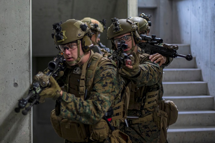 Marines carry rifles in an indoors environment.