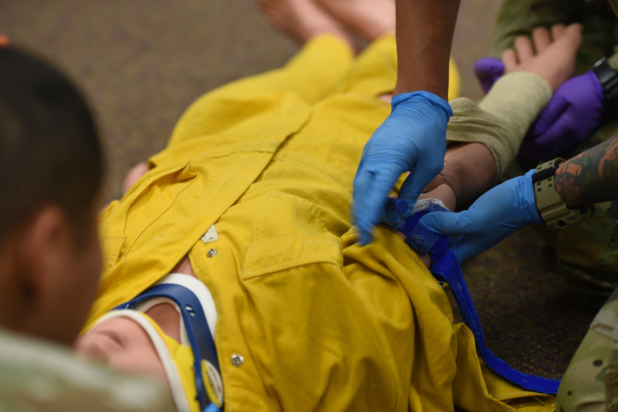 A joint service student assigned to the 312th Training Squadron, applies a cravat to a simulated victim’s upper extremity wound, during an Emergency Medical Responder psychomotor skills evaluation at Goodfellow Air Force Base, Texas, May 6, 2022. The training classrooms’ mobile chairs were rolled into the hallway to make room for the hands-on evaluation. This adaptation was an innovative example of modernized technology used for state-of-the-art training. (U.S. Air Force photo by Senior Airman Abbey Rieves)