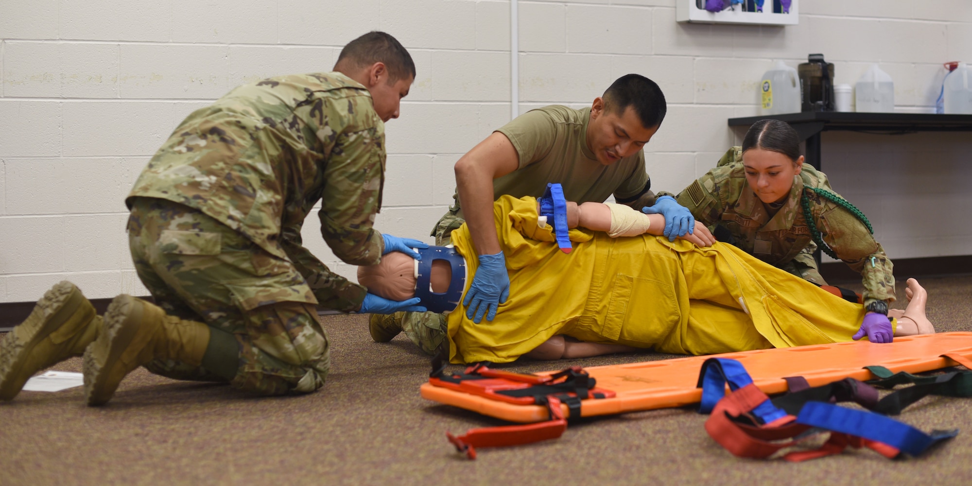 Joint service students assigned to the 312th Training Squadron, inspect the back of a simulated victim for injury, during an Emergency Medical Responder psychomotor skills evaluation at Goodfellow Air Force Base, Texas, May 6, 2022. EMR is a critical training objective at the Louis F. Garland Department of Defense Fire Academy because 90% of operational military emergency calls are EMR related. (U.S. Air Force photo by Senior Airman Abbey Rieves)