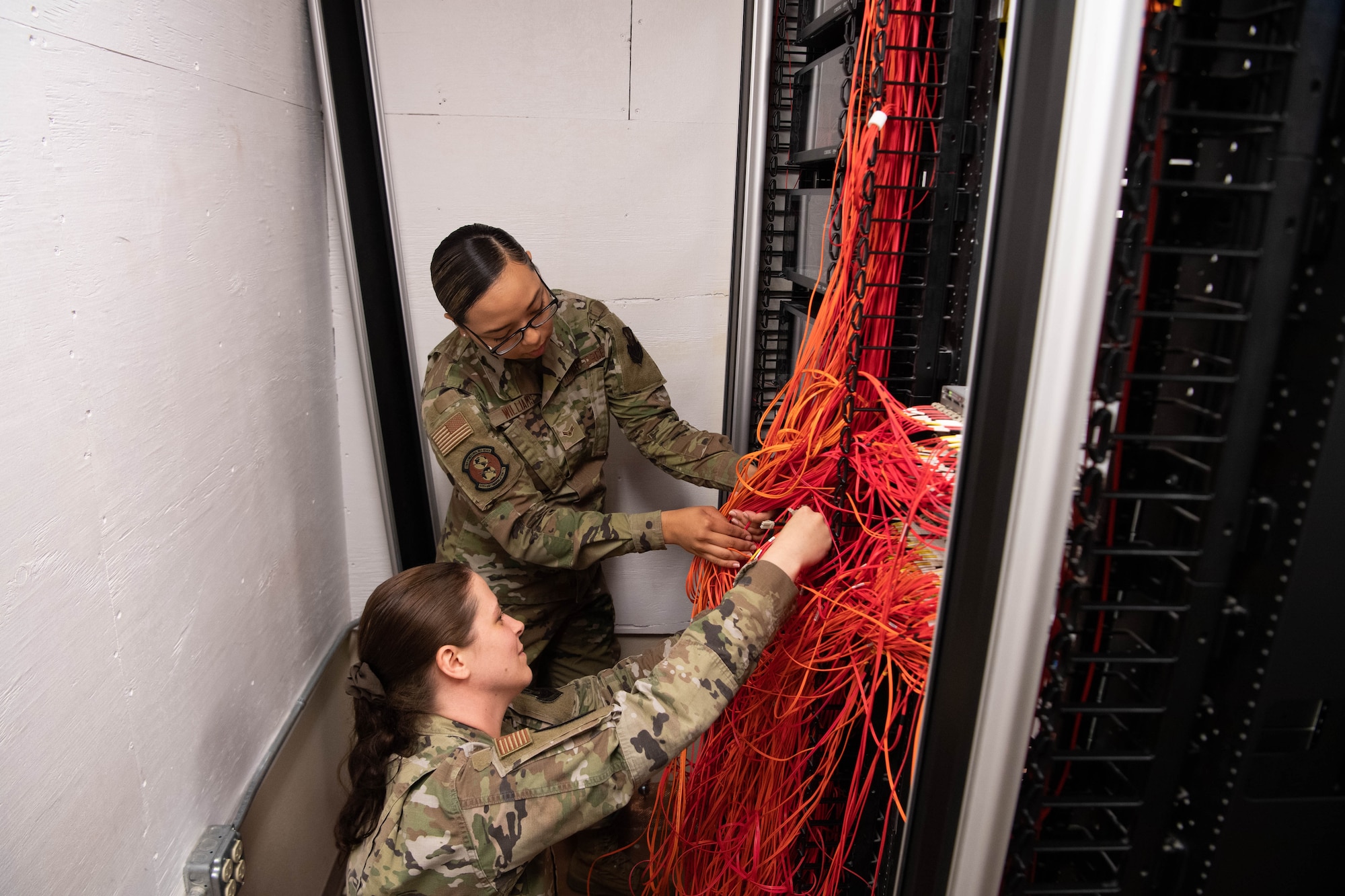 Airman 1st Class Sofaira Williams, 608th Air Communication Squadron network systems technician (top), and Airman 1st Class Victoria Montville, 608th ACOMS client systems technician (bottom), trace out connections in the ACOMS patch closet. The closet is used for troubleshooting network connectivity for users’ SIPR access. (U.S. Air Force photo by Staff Sgt. Bria Hughes)