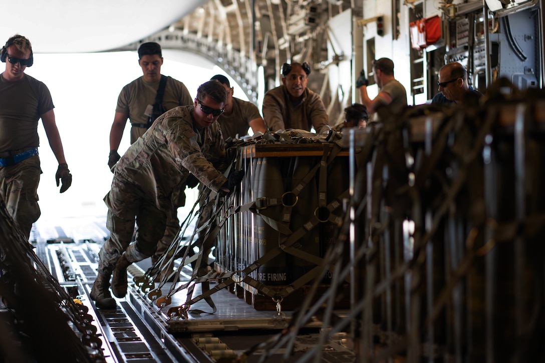 Several airmen push a pallet holding munitions into the cargo loading area of an airplane.