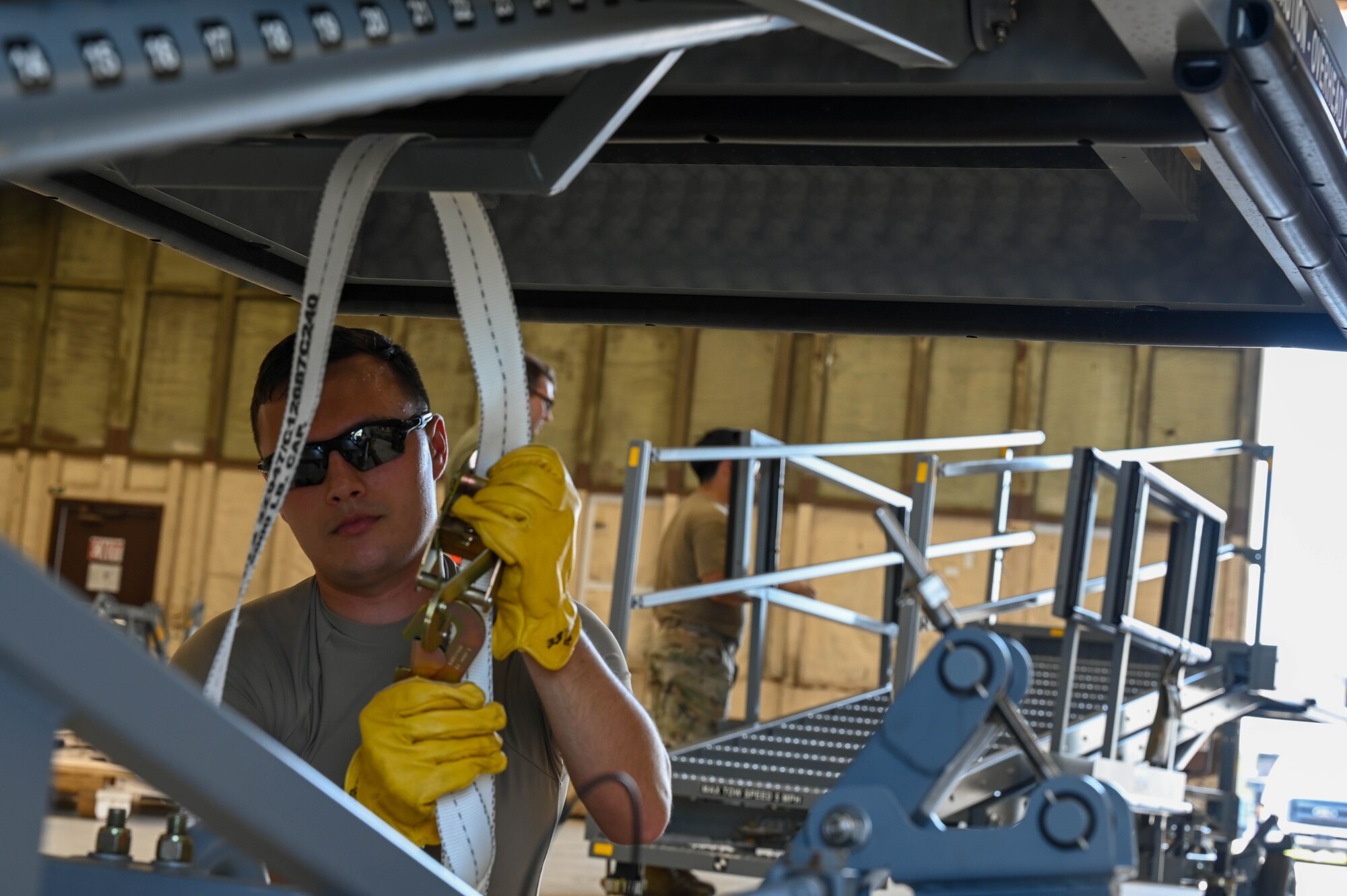 Airman preparing a B1 maintenance platform using straps while wearing yellow gloves.