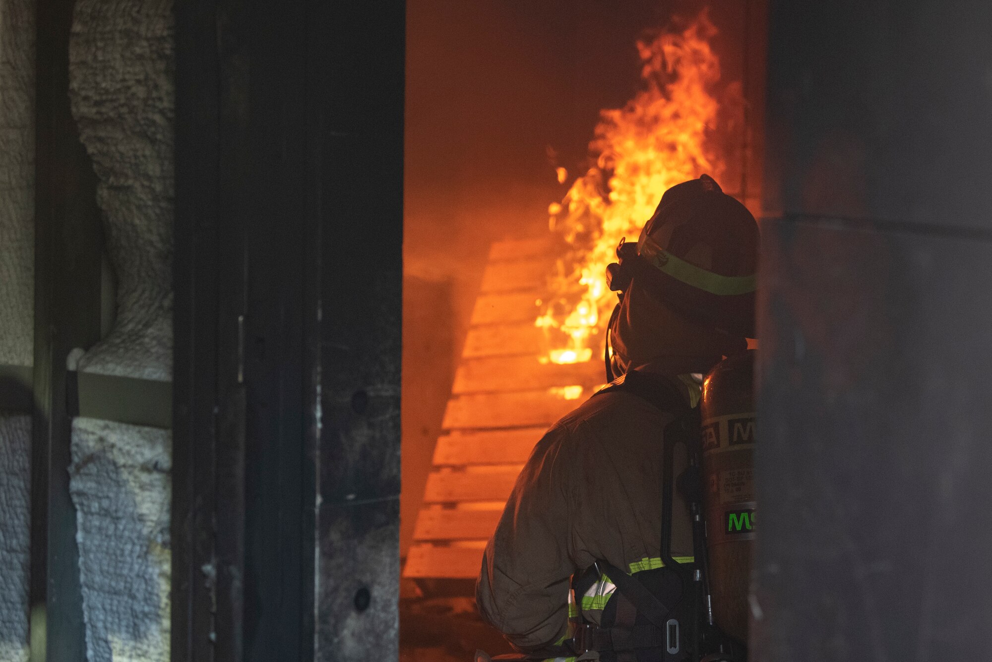 A photo of a man in a firefighter suit crouching down in front of a fire.