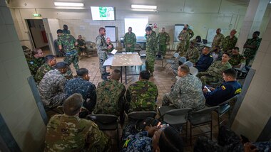 A group of military personnel look at a map during a briefing