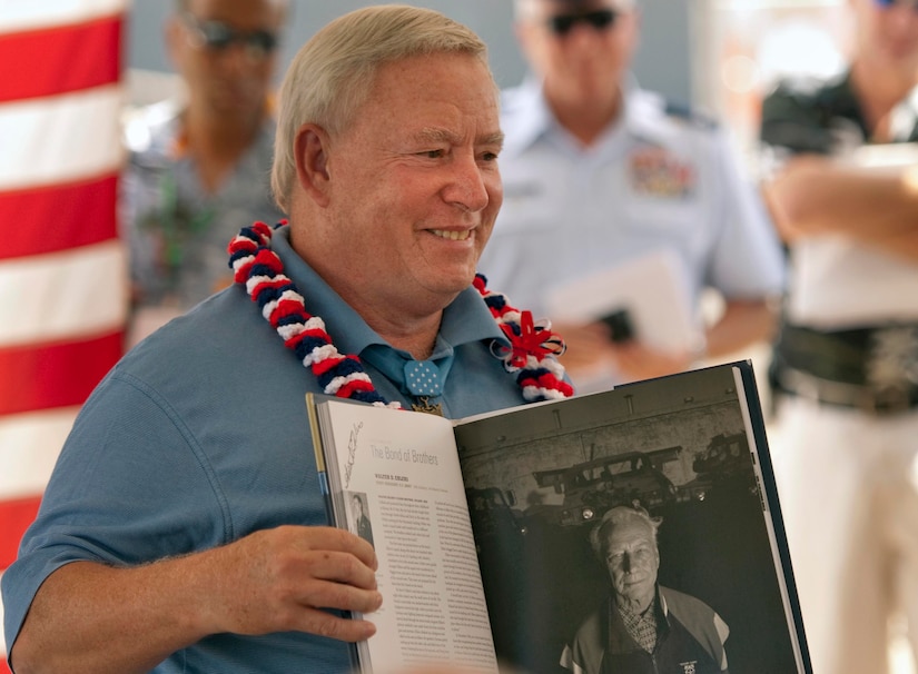 A smiling man wearing a Hawaiian lei holds open a book.