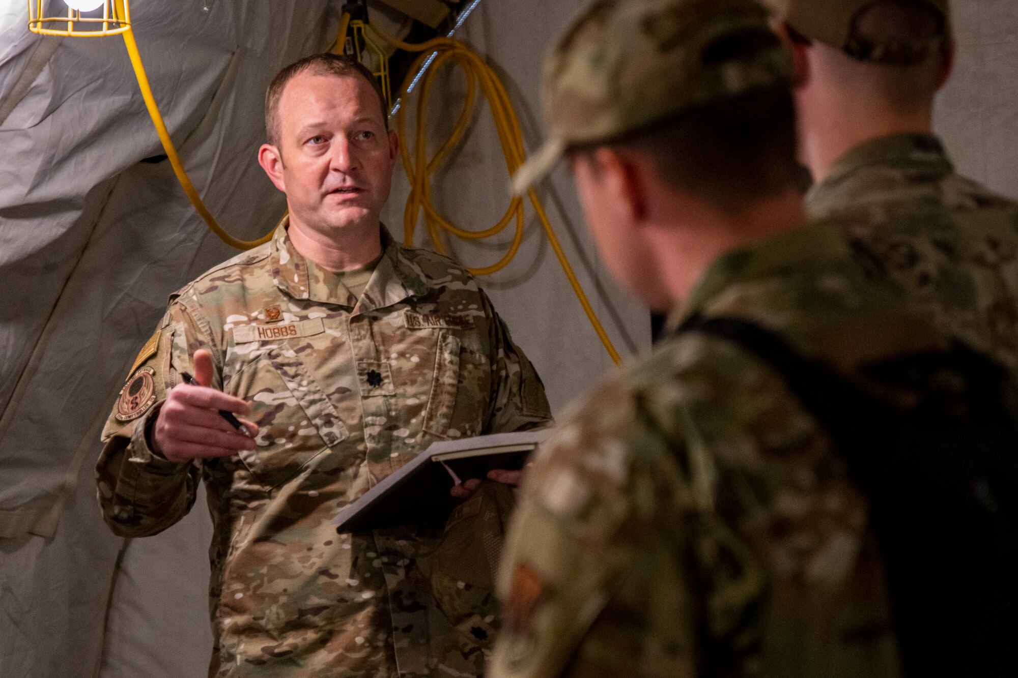 A photo of a group of Airmen standing inside a tent talking.
