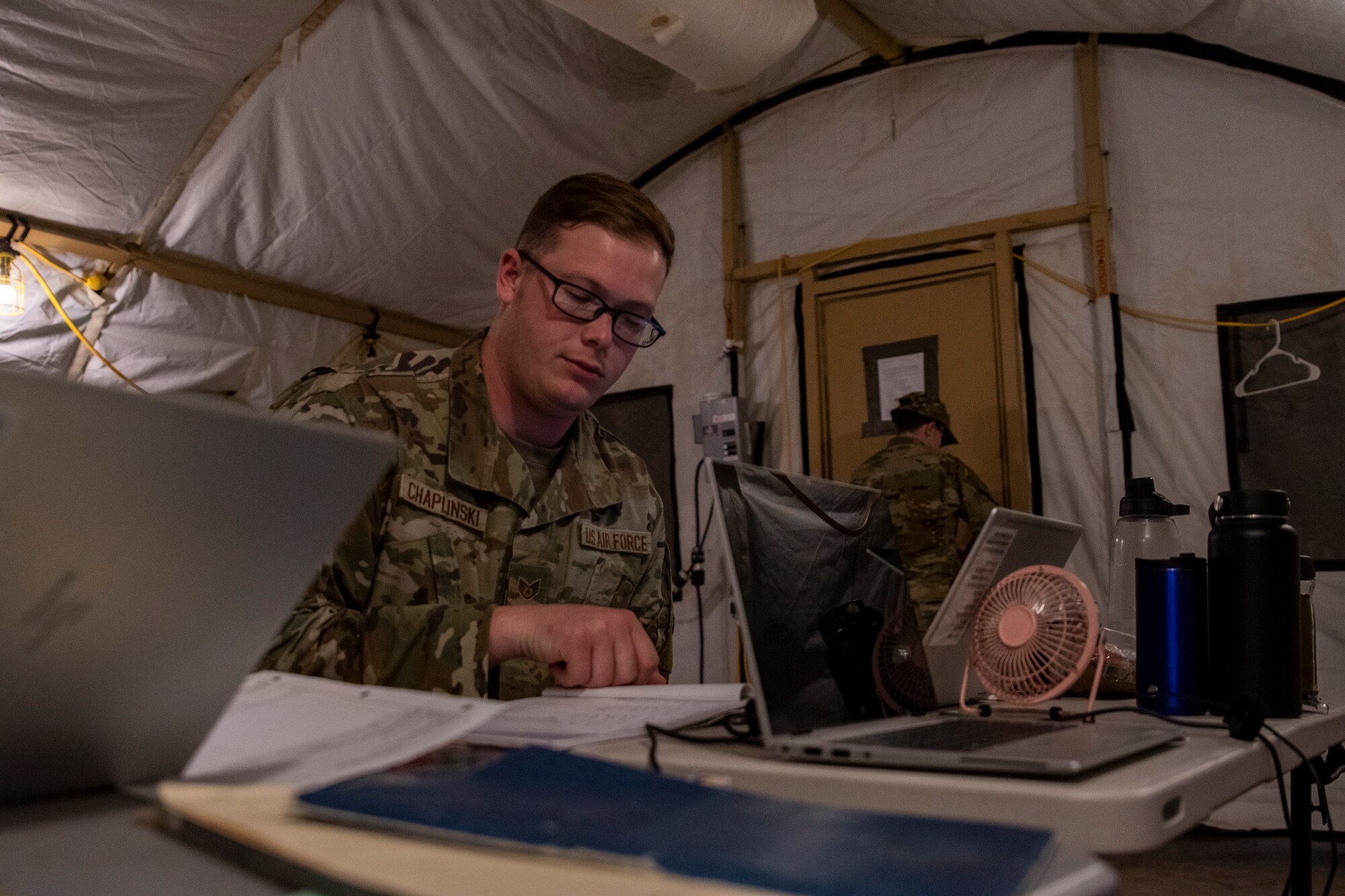 A photo of an Airman sitting at a table setup inside a tent looking through documents.