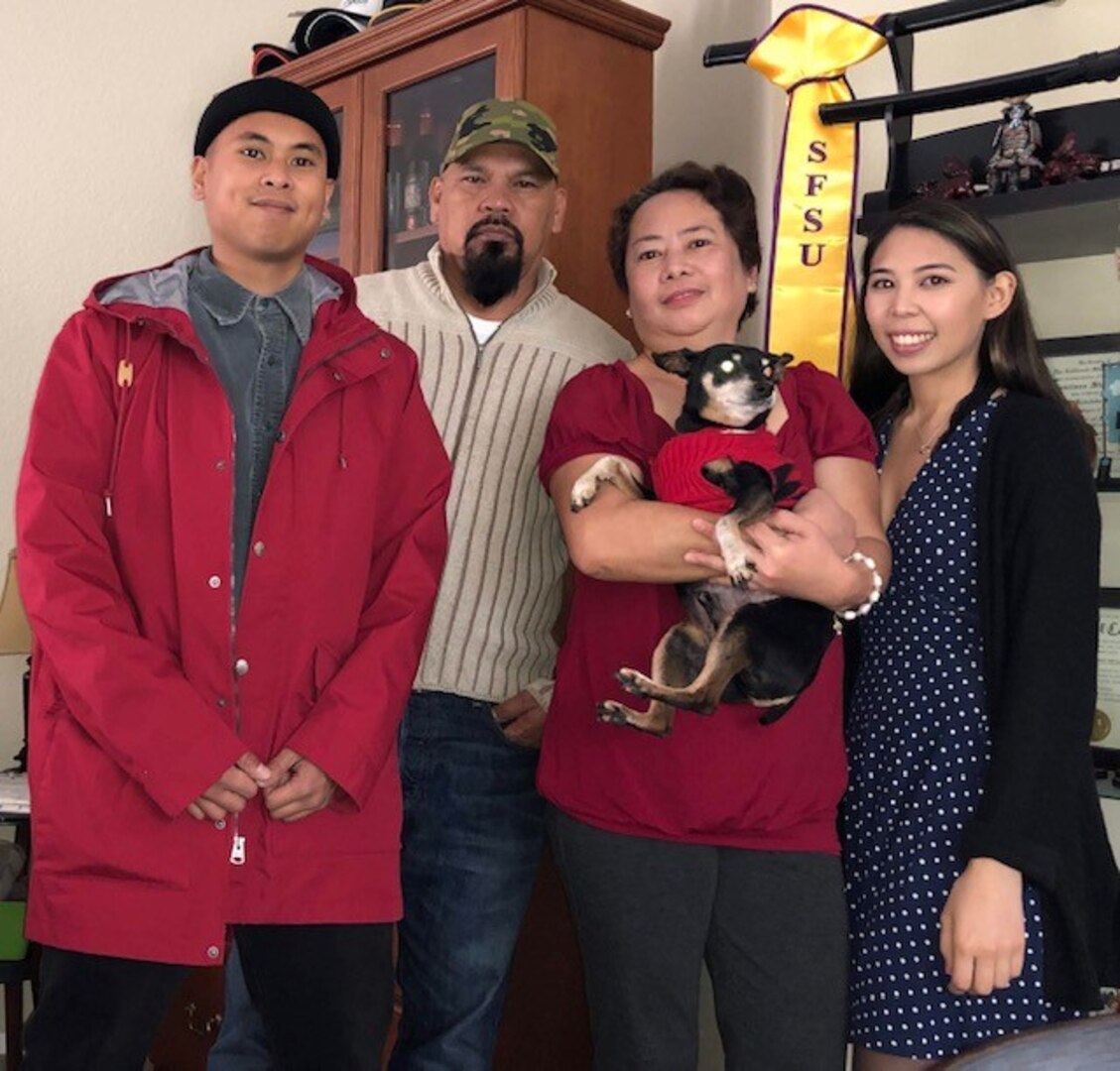 Man and woman standing with their two children and dog.