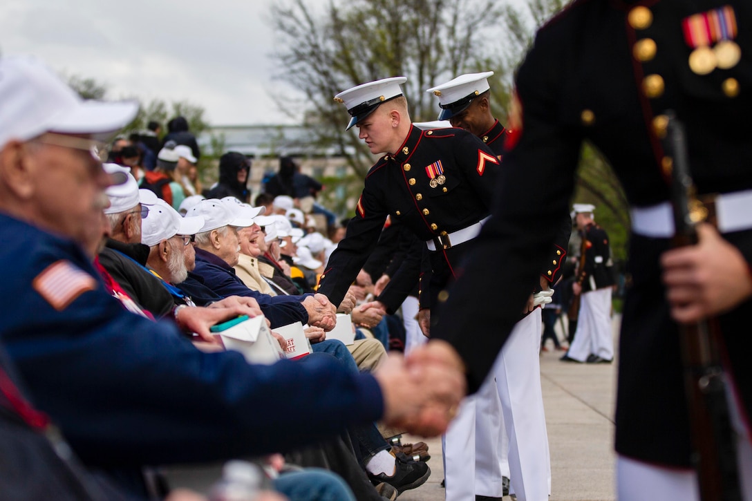 Marines shake hands with people sitting in a crowd.