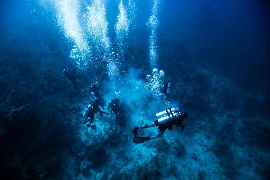 Soldiers wearing dive gear move underwater.