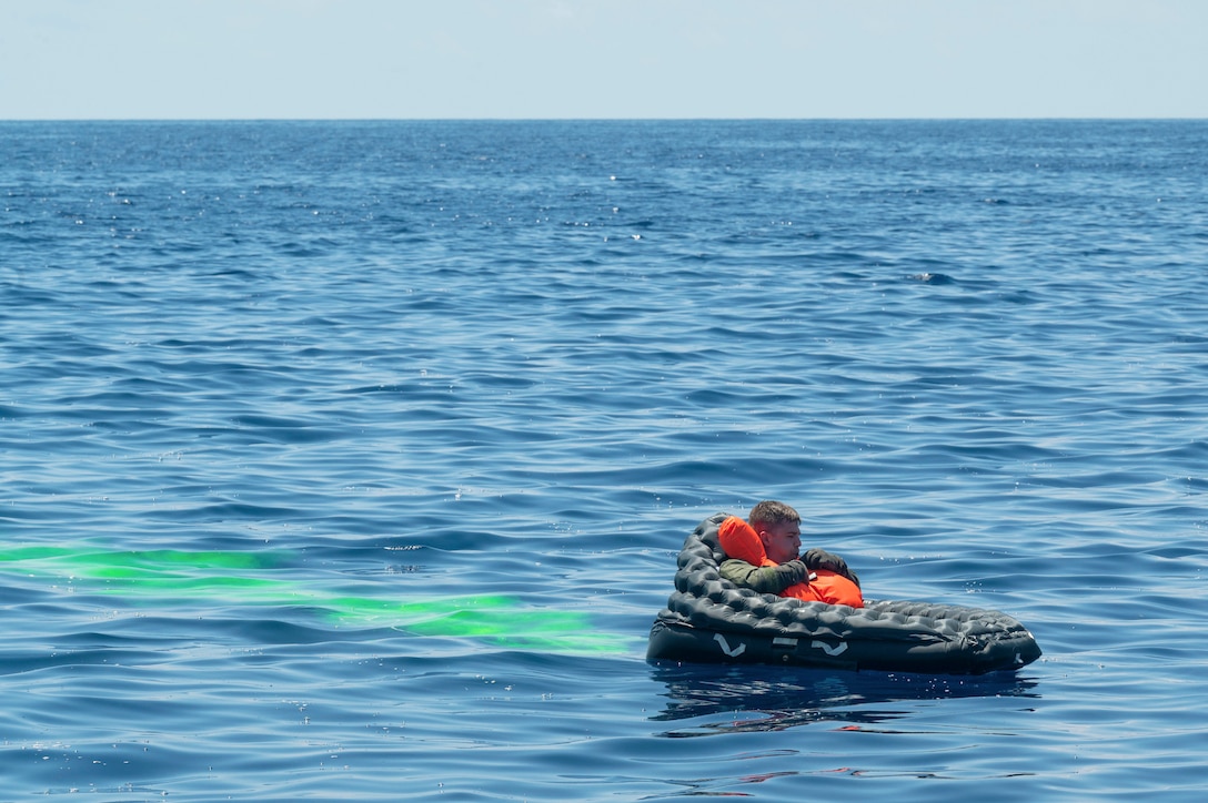 An airman inflates a life preserver in a body of water leaving behind a green streak.